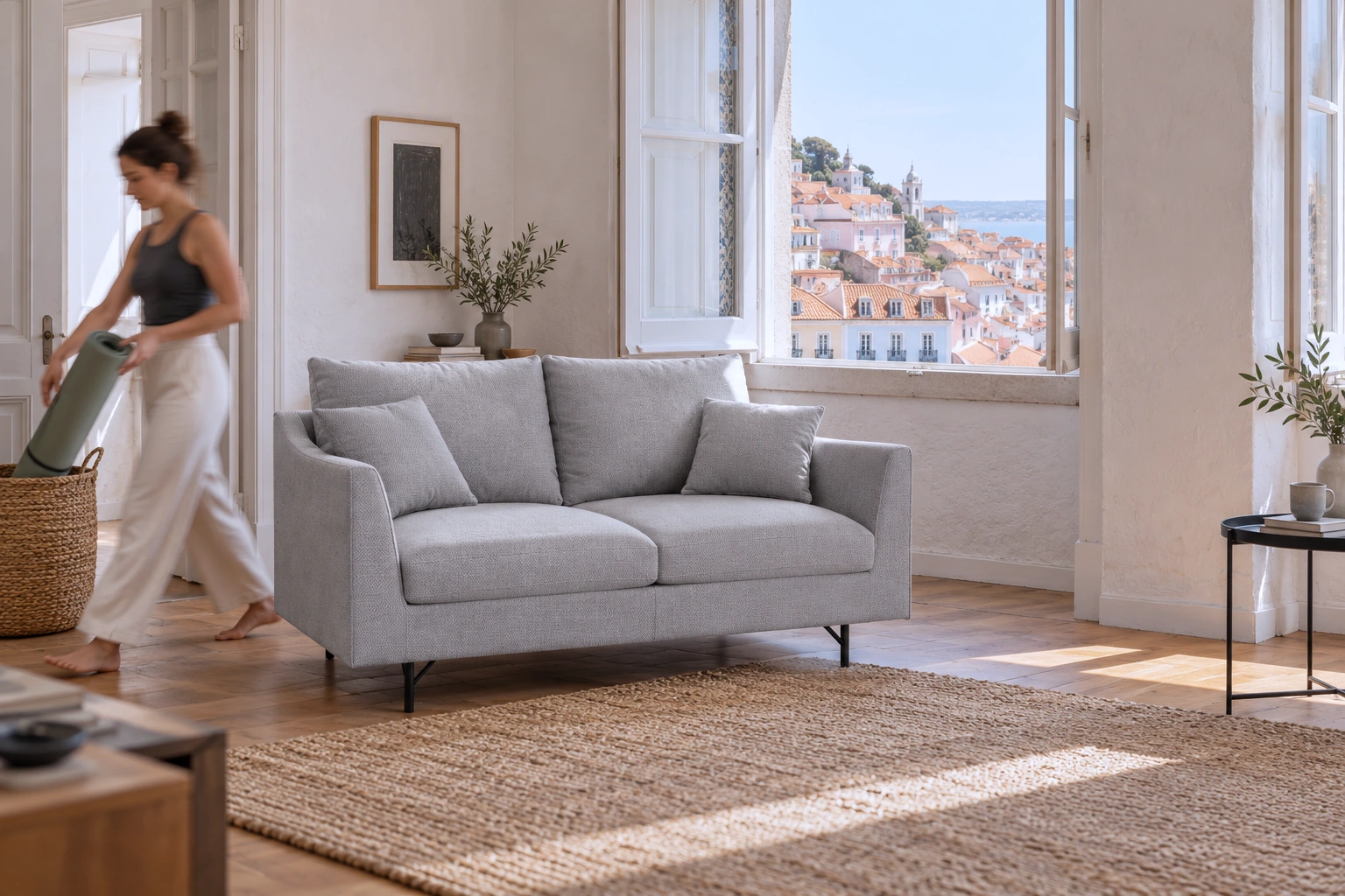 Grey ALFAMA sofa by a window overlooking Lisbon; a woman puts away a yoga mat