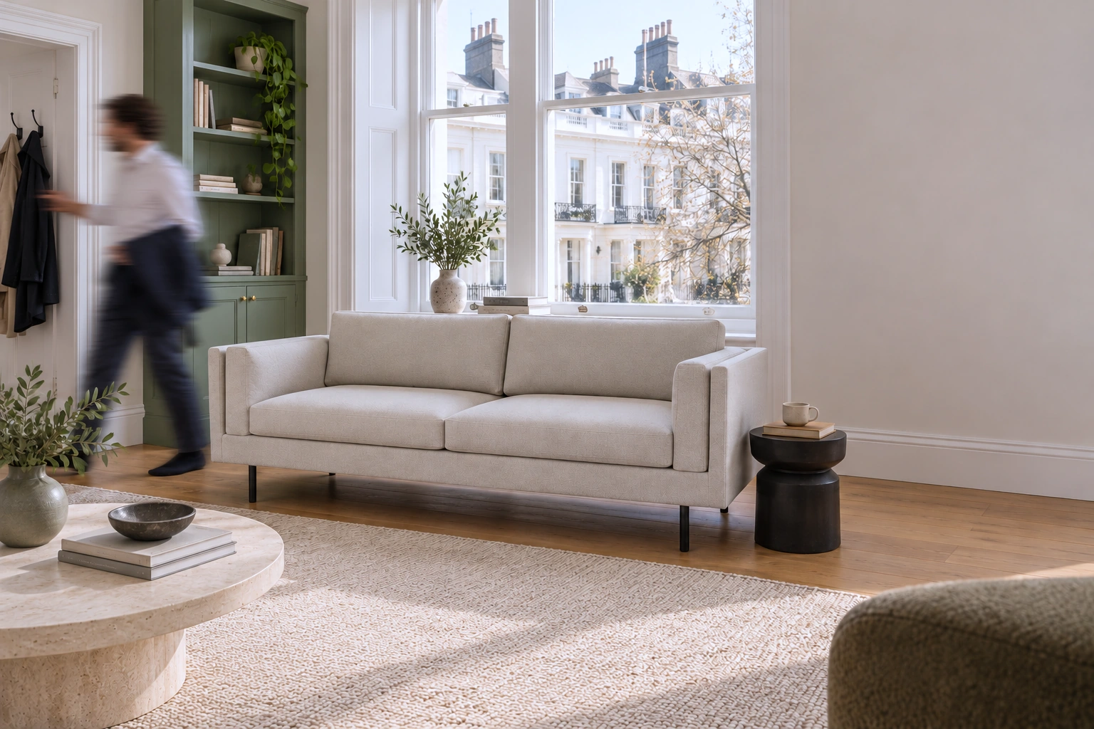 CHELSEA sofa by a London apartment window, with a person moving near the entrance