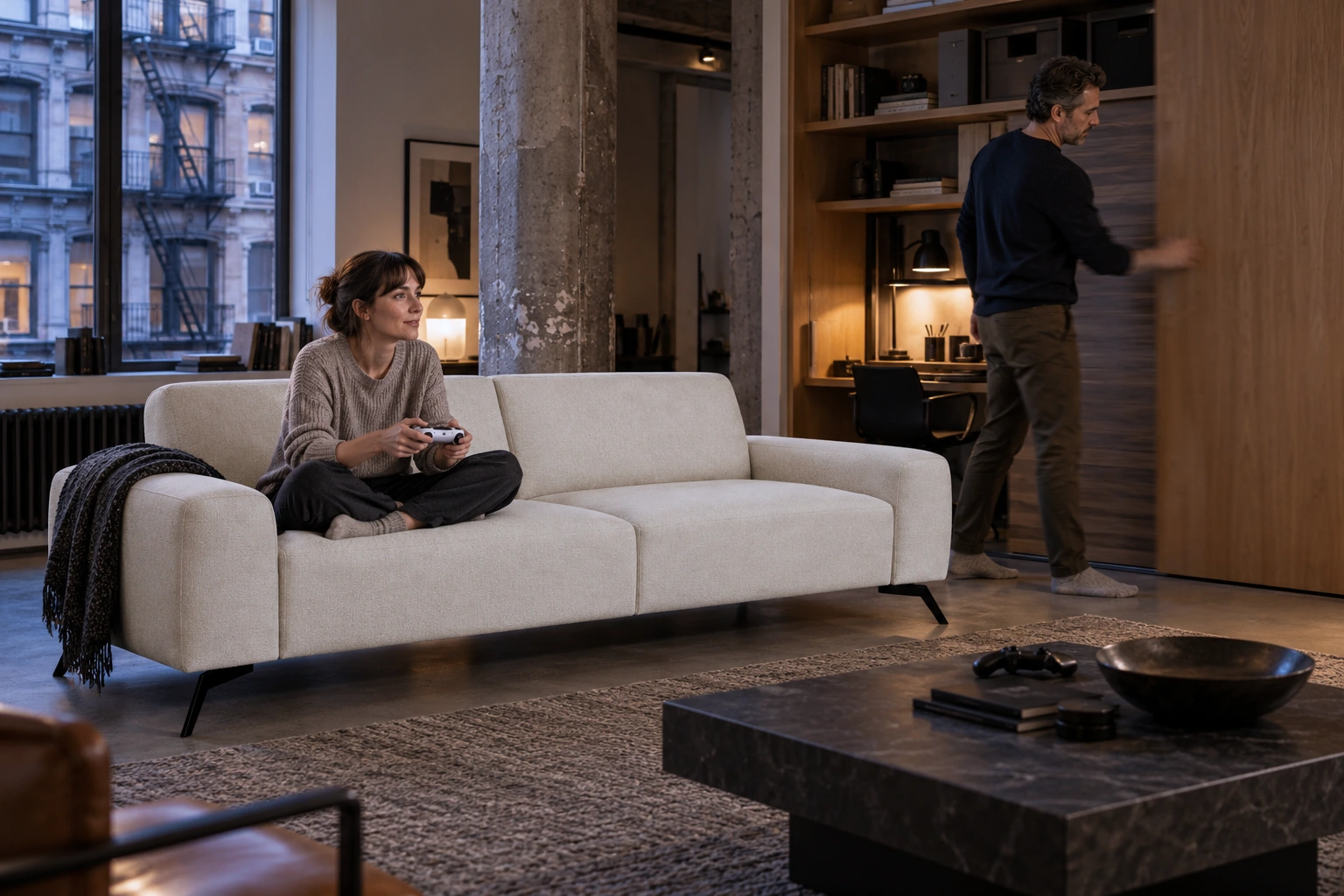 SOHO sofa in a New York interior; a woman plays a game while a man walks past the desk