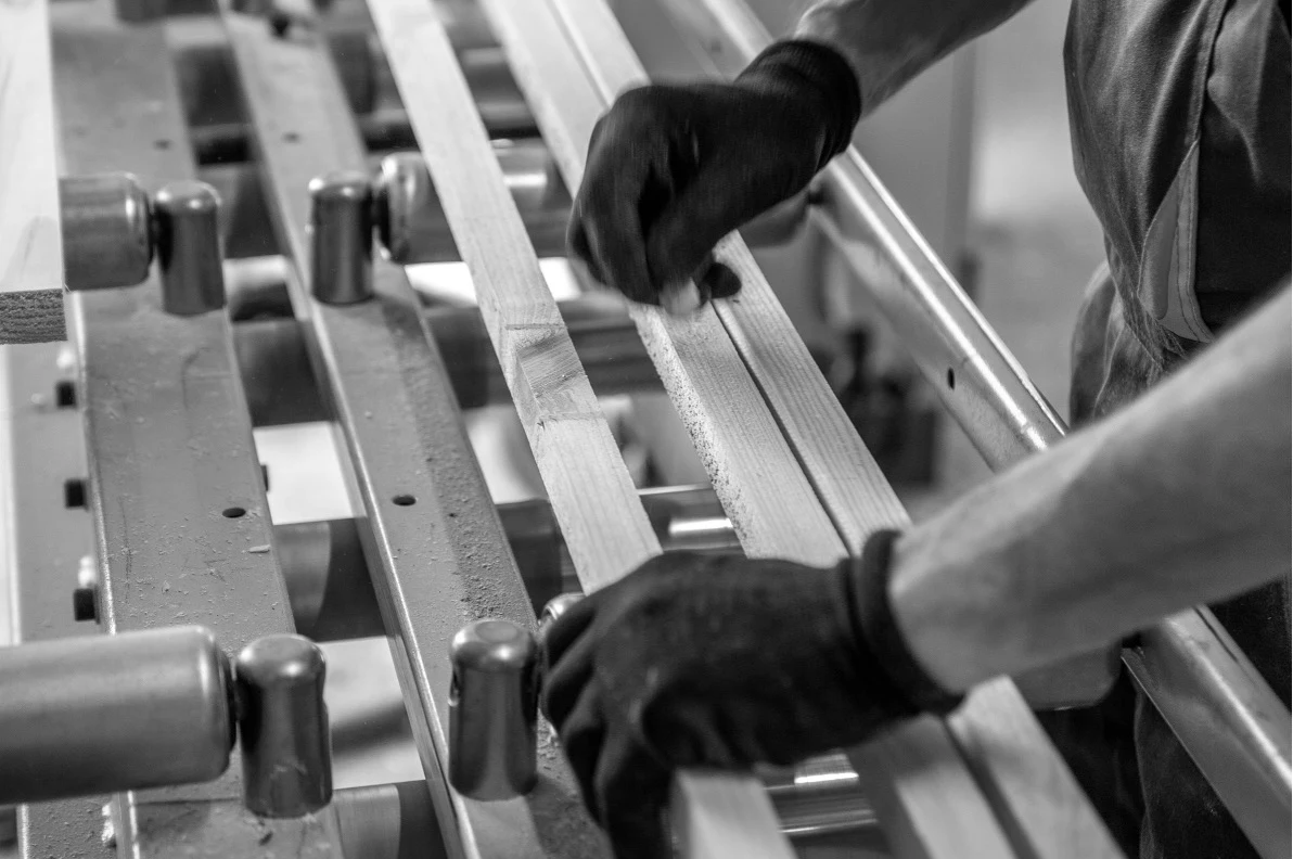 A worker&rsquo;s hands guiding wooden components through a machine
